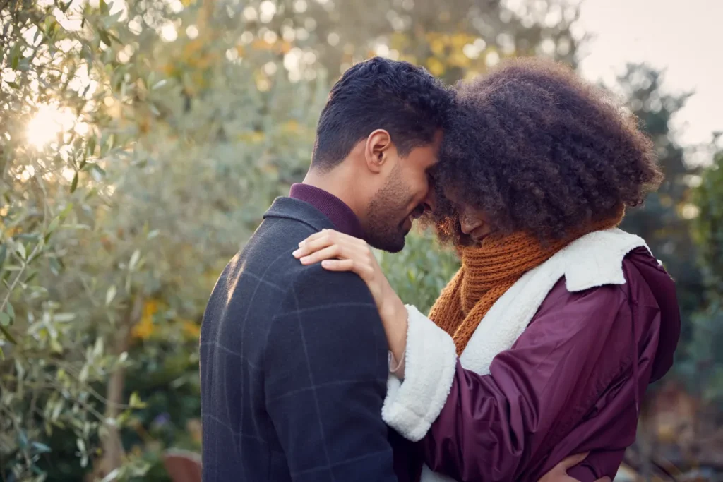 Pareja joven abrazada al aire libre, frente con frente, en un campo con luz de otoño