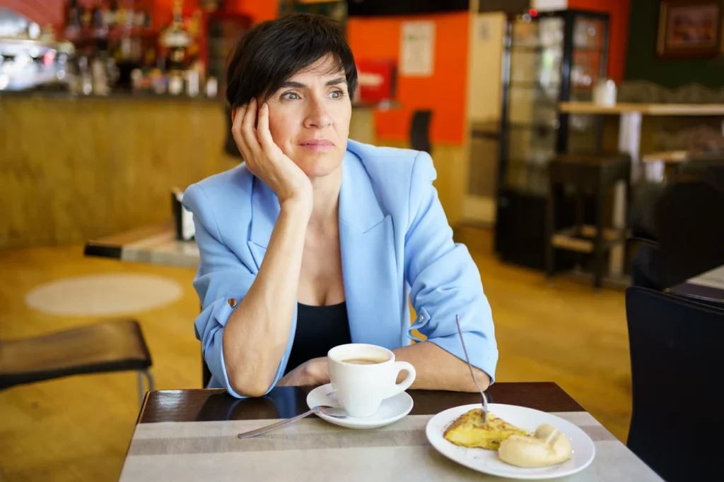 Mujer pensativa con una taza de café y el desayuno delante en una cafetería